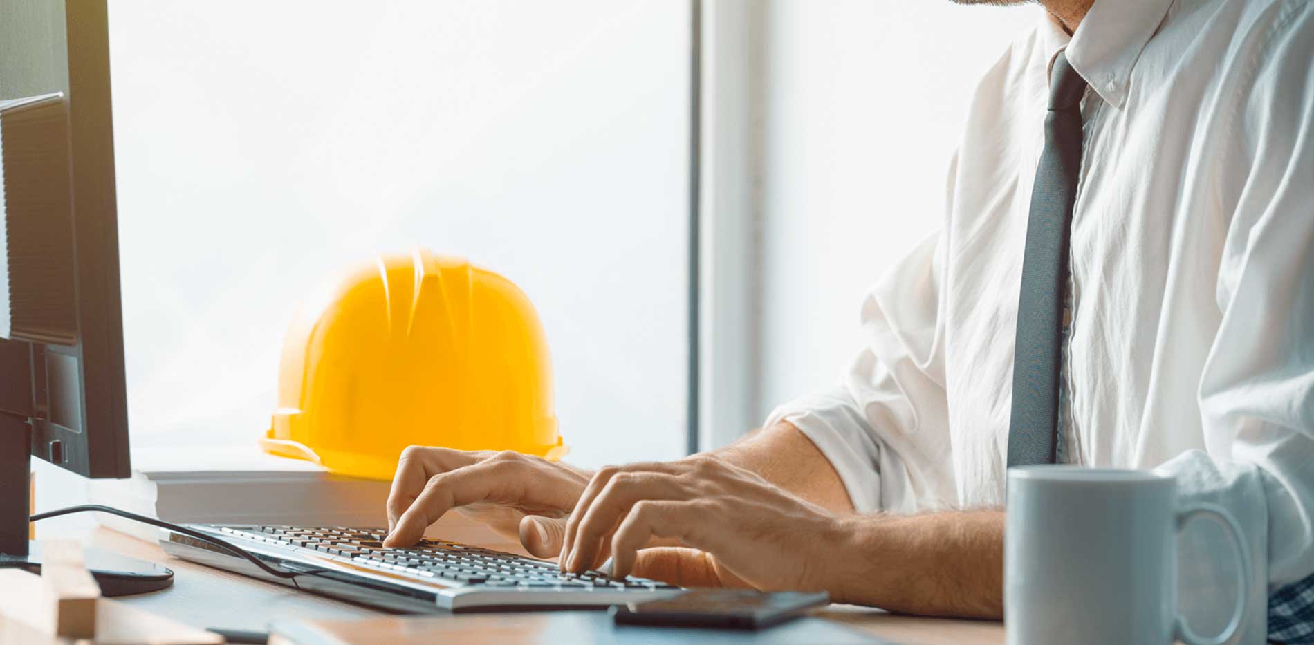Man working at desk with hard hat next to him